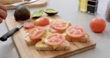 Mutfaktaki tahta kesme tahtasının üzerinde domates dilimli avokado tostu hazırlıyorum. Yemek, yemek, hazırlık, sağlıklı, vejetaryen, malzeme