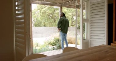 Verandada durmuş, Afro-Amerikan adam kahvenin tadını çıkarıyor ve bahçe manzarasına bakıyor. Rahatlama, sabah, açık hava, yaşam tarzı, boş zaman, doğa.