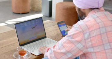İnternetten seyahat rezervasyonu, dizüstü bilgisayar ve akıllı telefon kullanan bir adam. Online rezervasyon, teknoloji, rahatlama, internet, gezinme, gelişigüzel