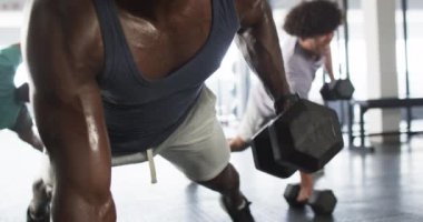 Koyu renk kolsuz bluz giyen, spor salonunda eğitim görmüş Afrikalı Amerikalı bir genç. Kısa siyah saçları var ve güçlü, formda, antrenmanına odaklanmış, değişmemiş, ağır çekimde