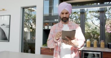 Tablet kullanarak, türbanlı adam modern evde duruyor, ekrana konsantre oluyor. Teknoloji, dijital, odaklanmış, konsantrasyon, kapalı alan, yaşam tarzı