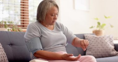 Tansiyonunu kontrol ediyorum, yaşlı kadın koltukta oturup sağlığına odaklanıyor. Sağlık, sağlık, izleme, yaşlılık, hipertansiyon, ev