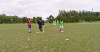 Çok ırklı erkek futbolcular antrenman yapıyor, topun peşinden koşuyor ve sahada engellerden kaçınıyor. spor, yaşam tarzı, takım çalışması, futbol ve etkinlik.