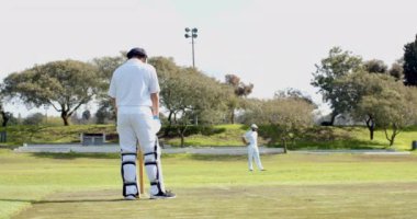 Kriket oynayan çok ırklı erkek kriket oyuncularından oluşan iki takım topu sahaya fırlatıyor. Spor, etkinlik, takım çalışması, rekabet ve kriket.