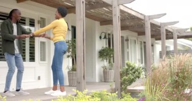 Gülümseyen Afrikalı Amerikalı çift anahtarlarını tutuyor, verandada yeni ev sahipliğini kutluyorlar. Ev sahipliği, kutlama, mutluluk, gayrimenkul, taşınma, açık hava