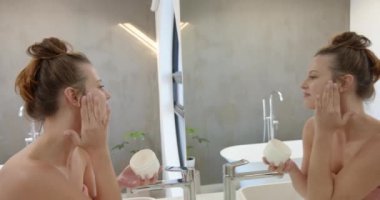 Yüz kremi sürüyorum, genç bir kadın modern banyoda aynaya bakıyor. Cilt bakımı, güzellik, kendine bakım, şımartma, sağlık, bakım.