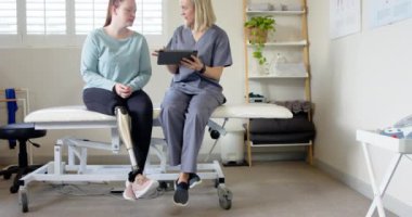 Protez bacaklı bir kadın terapistle terapi planını tartışıyor. Tablet kullanıyor, kopyalama alanı kullanıyor. Fizyoterapi, rehabilitasyon, sağlık, tıbbi, protez, terapi