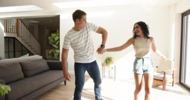 Birlikte dans eden, genç, çok ırklı çift aydınlık oturma odasında, evde eğleniyor. Dans, mutluluk, ev, yaşam tarzı, hareket, romantizm