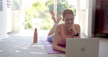 Yoga minderinde yatmak, evde dizüstü bilgisayar ve su şişesi kullanan bir kadın. Fitness, sağlık, teknoloji, yaşam tarzı, susuzluk, ev çalışması, değişmemiş,