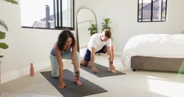 Yoga çalışmalar, evdeki parlak yatak odasındaki paspasların üzerinde gerinen genç, çok ırklı bir çift. Spor, sağlık, egzersiz, rahatlama, ev