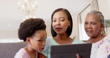 Tablet kullanarak, üç nesil boyunca Afro-Amerikan kadınları evde oturup gülümsediler. Afro-Amerikan ailesi, birliktelik, teknoloji, bağ, mutluluk.