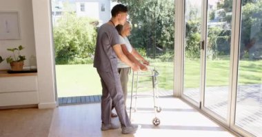 Fizyoterapist, Walker 'a parlak, güneşli odada yardımcı oluyor. Fizyoterapi, rehabilitasyon, sağlık hizmetleri, yaşlılar, hareketlilik, yardım