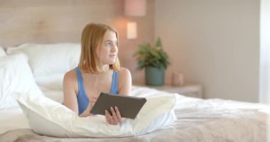 Yatakta dinlenen, evde kitap okuyan ya da gezen bir kadın. Rahatlama, teknoloji, rahatlık, yaşam tarzı, kapalı alan, yatak odası, değişmemiş,