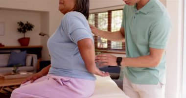 Fizyoterapist oturma odasında sırt egzersizleri yapan yaşlı bir kadına yardım ediyor. Rehabilitasyon, sağlık, fizyoterapi, sağlık, terapi, iyileşme