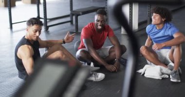 Spor salonunda oturup gülümseyen bir grup genç adam. Bir güçlü ve formda Afro-Amerikan adam, iki formalı siyah-mavi gömlekli, değiştirilmemiş, ağır çekim