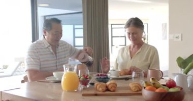 Kahvaltının tadını çıkarıyor, kıdemli çift masada kruvasan ve meyveyle oturuyor. Aile, yaşam tarzı, yemek, yaşlılar, sağlıklı, yemek, değişmemiş, yavaş çekim