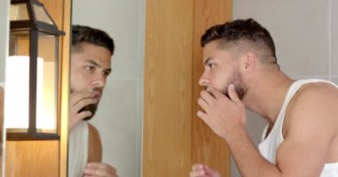 Sakal uzatma, evdeki banyo aynasında yansımayı inceleyen adam. Tıraş, kişisel bakım, hijyen, günlük rutin sakal bakımı, sabah rutini.