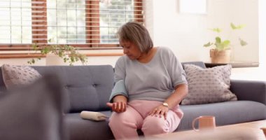 Kan basıncına bakıyorum, oturma odasındaki kanepede oturan yaşlı kadın. Sağlık, sağlık, izleme, ev bakımı, yaşlılar, yaşam tarzı