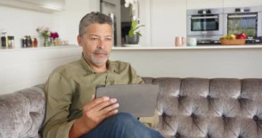 Modern evdeki kanepede dinlenirken tablet kullanan gülümseyen adam. Teknoloji, rahatlama, rahatlama, dijital, yaşam tarzı, konfor