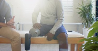 Protez bacaklı bir adam masada oturmuş, klinikte terapistle konuşuyor. Rehabilitasyon, sağlık, fizyoterapi, protez, konsültasyon, tıbbi tedavi