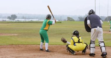 Çok ırklı bayan beyzbol oyuncuları ve erkek hakem, beyzbol sopasıyla topa vuruyorlar ve sahada koşuyorlar. Spor, etkinlik, takım çalışması, rekabet ve beyzbol.