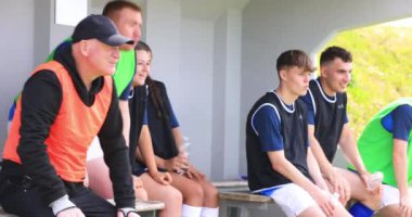 Erkek ve bayan futbolcular yedek kulübesinde oturuyor, bağırıyor ve sahada koçla destek oluyor. spor, yaşam tarzı, takım çalışması, futbol ve etkinlik.