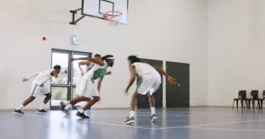 Bir grup çok ırklı erkek basketbolcu spor salonunda koşuyor ve ısınıyor, koç gözlemliyor. spor, yaşam tarzı ve etkinlik.