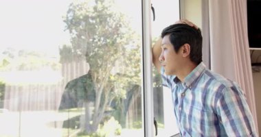 Pencereden dışarı bakıyor, ekose gömlekli Asyalı adam yansıyor, el kafaya, fotokopi uzayı. Düşünmek, düşünmek, düşünmek, yalnızlık, düşünmek, ev içinde