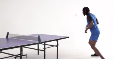 Beyaz arka planda servis yapan ve pas veren Afro-Amerikan masa tenisçisi. Spor, etkinlik, takım çalışması ve masa tenisi.