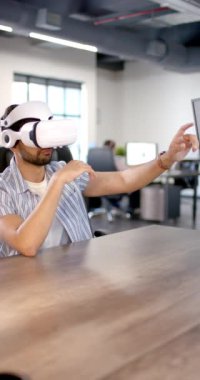 Dikey video: VR kulaklık kullanan bir adam modern ofisteki sanal arayüzle etkileşime geçiyor. Teknoloji, yenilik, sanal gerçeklik, iş adamı, çalışma alanı, dijital