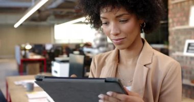 Modern ofiste tablet kullanan melez bir kadın, iş arkadaşlarıyla açık çalışma alanı. İş hayatına gelişigüzel bir girişimci olarak başlamak, arka planda işbirliği yapmak, yavaş çekim...