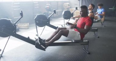 Beden eğitiminde kürek çeken bir grup genç adam. Kırmızı tişörtlü ve beyaz şortlu Afro-Amerikan bir adam ve siyah-mavi gömlekli iki çift ırklı adam, hepsi spor yapmaya odaklanmış, değişmemiş.