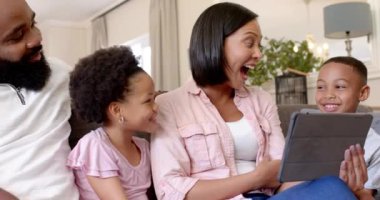 Afro-Amerikan ailesi kanepede oturuyor, anne çocuklu tablet kullanıyor, kaliteli zaman geçiriyor. Bağlanma, oturma odası, teknoloji, ebeveynlik