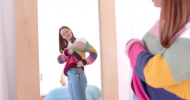 Aynaya bakan, kazağı ve kotu ayarlayan, kendine güvenen bir kadın. Moda, giysi, yansıma, güven, uyum, tarz