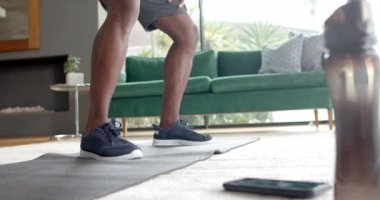 Yoga minderinde egzersiz yapan, spor ayakkabılı Afro-Amerikan bir adam evde esniyor. Fitness, egzersiz, antrenman, ev çalışması, atletizm, değişmemiş, yavaş çekim