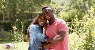 Açık havada kucaklaşan, güneşli bahçede eğlenen gülümseyen Afrikalı Amerikalı çift. Romantizm, mutluluk, aşk, birliktelik, güneş ışığı, sevgi
