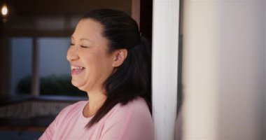 Gülümseyen olgun bir kadın kapı çerçevesine yaslanıyor, evde rahat bir anın tadını çıkarıyor. Yaşam tarzı, rahatlık, rahatlama, mutluluk, konfor, kapalı alan