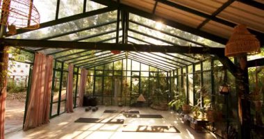 Güneş ışığı, minderleri ve bitkileri olan cam ev yoga stüdyosuna akıyor. Sağlık, rahatlama, fitness, zen, huzurlu, egzersiz