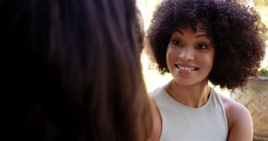 Kıvırcık saçlı, gülen kadın dışarıda başka biriyle konuşuyor. sohbet, mutluluk, iletişim, arkadaşlık, sosyal, yaz