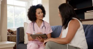 Pembe önlüklü hemşire kanepede oturan kadına tablet gösteriyor, sağlığı tartışıyorlar. Sağlık, danışma, hemşirelik, hasta, tartışma, meslek