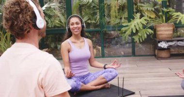 Kulaklık takan, cam evde yoga minderi üzerinde meditasyon yapan bir kadın. Meditasyon, farkındalık, rahatlama, sükunet, zen, sağlık