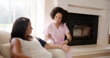 Pembe önlüklü hemşire koltukta oturan kadının tansiyonunu ölçüyor. Sağlık, hemşirelik, sağlık, hasta, muayene, evde bakım