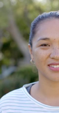 Dikey video: Çilli ve halka küpeli gülümseyen kadın açık havada eğleniyor. Portre, mutluluk, yaz, doğa, aksesuarlar, rahatlama