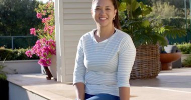 Gülümseyen kadın dışarıda oturuyor, arka planda bitkilerle güneşli bir günün tadını çıkarıyor. Güneş ışığı, doğa, yaz, mutluluk, rahatlık, rahatlama.