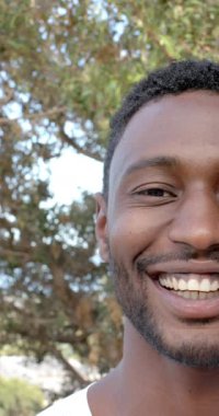 Dikey video: Arka planda ağaçlarla gülen adam, doğanın ve temiz havanın tadını çıkarıyor. Rahatlama, mutluluk, yaşam tarzı, yeşillik, rahatlık