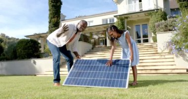 Güneş paneli kuruyor, baba ve kızı ön bahçede birlikte çalışıyor. Yenilenebilir enerji, aile, takım çalışması, sürdürülebilirlik, yeşil enerji, çevre