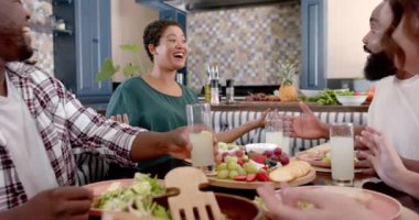 Bir grup arkadaş birlikte yemek yiyor, gülüyor ve evde içkilerini paylaşıyorlar. Yemek, sosyalleşme, kahkaha, yemek, içecekler, değiştirilmemiş, yavaş çekim