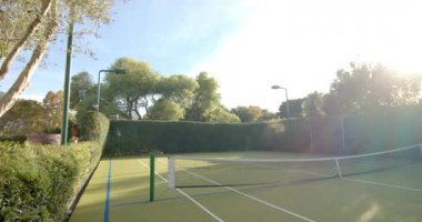 Güneş ışığı ağaçlarla çevrili boş tenis kortunda parlıyor. Açık satırları ve ağı gösteren mahkeme, oyun için davet, değiştirilmemiş, yavaş çekim