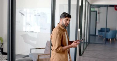 Tableti tutan, gülümseyen ve modern ofis koridorunda yürüyen bir adam. İş adamı, teknoloji, profesyonel, kurumsal, işyeri, dijital