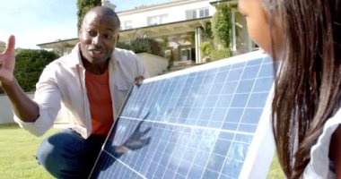Güneş paneli kurulumunu açıklayan Afro-Amerikan erkek arka bahçedeki kadına yenilenebilir enerji veriyor. Sürdürülebilirlik, yeşil enerji, çevre dostu teknoloji, çevre, elektrik